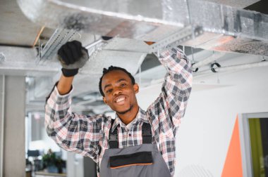 Genç Afrikalı Amerikalı işçi havalandırma sistemini tamir ediyor, Hvac ekipmanlarının bakımını yapıyor.