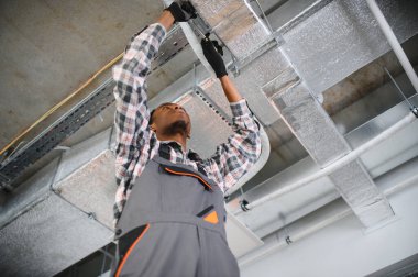 Genç Afrikalı Amerikalı erkek teknisyen endüstriyel havalandırma sistemini tamir ediyor, Hvac ekipmanları üzerinde bakım yapıyor.