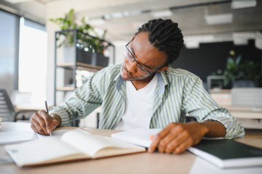 Gözlüklü kendini adamış bir öğrenci, kitaplarla çevrili bir üniversite kütüphanesinde yoğun bir şekilde okuyor, tıp diploması ve geleceğin mezuniyetini hedefliyor.