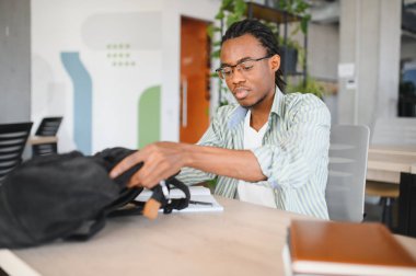 Genç odaklı Afrikalı Amerikalı öğrenci not alıyor ve üniversite kütüphanesinde okumaya hazırlanıyor.