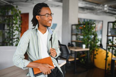 Modern bir üniversite ortamında, elinde bir kitapla, kendini derslere ve gelecekteki mezuniyete adamış genç bir Afrikalı Amerikalı öğrenci.