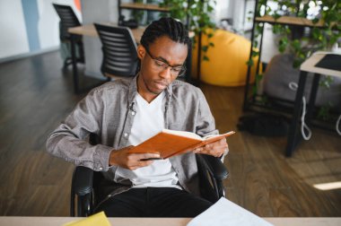Özürlü genç bir adam kitap okuyor, okuyor, üniversitede eğleniyor, modern bir ofiste çalışıyor.