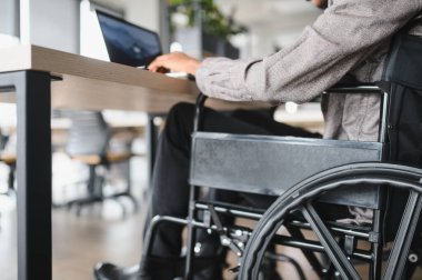 Modern ofiste dizüstü bilgisayar kullanan kendine güvenen genç profesyonel, iş yerinde entegrasyon ve ulaşılabilirlik gösteriyor