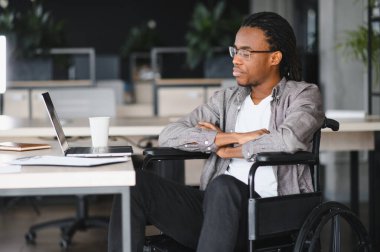 Engelli genç işadamı erişilebilir ofiste bilgisayar kullanarak çalışıyor, güven ve kararlılık gösteriyor