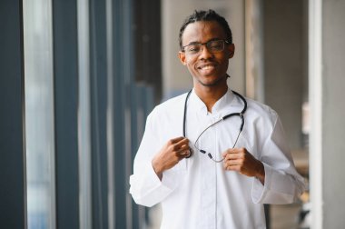 Kendine güvenen genç bir Afro-Amerikan erkek doktorun portresi gülümseyen ve steteskop tutan, sağlık ve tıbbi uzmanlığı temsil eden