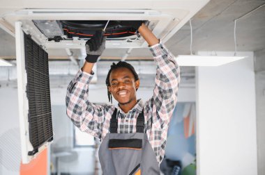 Gülümseyen Afro-Amerikan işçiler içeride havalandırma sistemini tamir ederken, en uygun soğutma ve konforu sağlamak için tornavida kullanıyorlar.