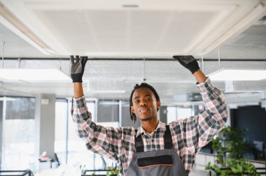 Genç Afrikalı Amerikalı işçi parlak bir ofise havalandırma sistemi kuruyor.