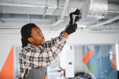 Genç Afro-Amerikan işçiler, kilit anahtarı kullanarak havalandırma sistemini tamir ediyorlar.