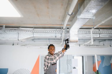 Genç Afro-Amerikan HVK teknisyeni modern bir binaya havalandırma ve iklim kontrolü sağlayan bir havalandırma sistemi kuruyor.