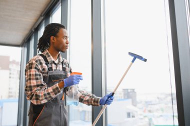 Modern bir ofis binasında havalandırma ve havalandırma bakımı üzerine yoğunlaşarak büyük pencereleri temizlemek için araç kullanan Afrikalı Amerikalı işçiler