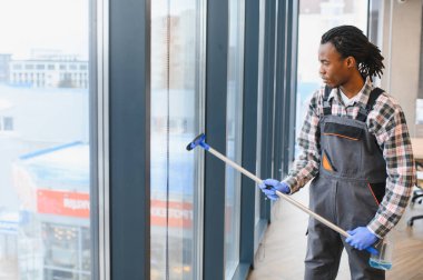 Modern bir ofis binasının camlarını temizleyen genç adam, profesyonel ekipmanlardan faydalanıyor ve aynı zamanda temiz hava sağlıyor.