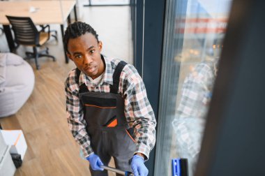 Modern bir ofis binasının camlarını profesyonel ekipmanlarla temizleyen Afrikalı Amerikalı genç bir işçi.
