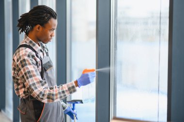 Profesyonel bir işçi büyük cam pencereleri temizlemek için sprey kullanıyor. Ticari bir ortamda bakım ve temizlik konusunda uzmanlık gösteriyor.