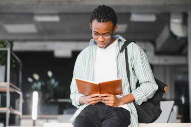 Üniversite kütüphanesinde okuyan genç siyahi bir adam, bir ders kitabı okumaya ve akademik başarı için bilgiyi özümsemeye derinden odaklanmış.