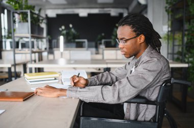 Tekerlekli sandalyede yazı yazarak ve modern, parlak bir kütüphanede okuyarak engelli genç adam işine odaklandı.