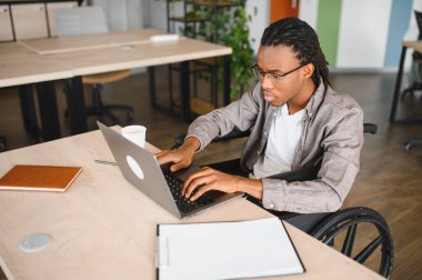 Özürlü genç adam, modern ofiste dizüstü bilgisayarla çalışıyor, işyerine dahil edilme ve erişilebilirlik gösteriyor