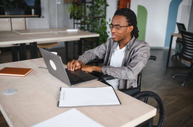 Özürlü, özgüvenli, bilgisayar kullanan, modern ofiste uzaktan çalışan Afro-Amerikan bir adam.