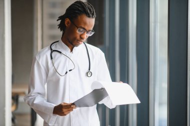Kendine güvenen genç Afrikalı Amerikalı doktor hastanın tıbbi kayıtlarını dikkatlice inceleyerek profesyonelliğini ve sağlık hizmetlerine bağlılığını gösteriyor.