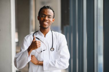 Laboratuvar önlüğü ve steteskop giyen kendine güvenen doktor olumlu jest gösteriyor ve sağlık hizmetlerinde başarı gösteriyor.