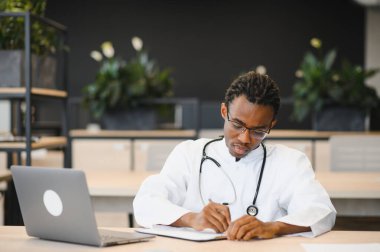 Yoğunlaştırılmış pratisyen, dizüstü bilgisayar, somutlaştırıcı profesyonellik ve sağlık uzmanlığı kullanarak tıp ofisinde notlar alıyor.