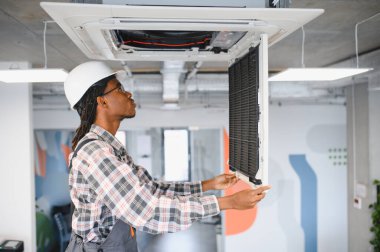 Modern bir ofiste klimayı ustalıkla tamir eden sıkı bir şapkalı teknisyen ideal havalandırma ve soğutma sağlıyordu.