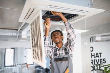 Modern bir ofis ortamında teknisyen, bir havalandırma ünitesini ustalıkla tamir ediyor, uygun havalandırma ve iklim kontrolü sağlıyor.