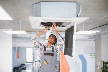 HVC teknisyeni, çağdaş bir ofis alanında bakım ve onarım yapan bir tavan monte edilmiş klima ünitesi üzerinde çalışıyor.