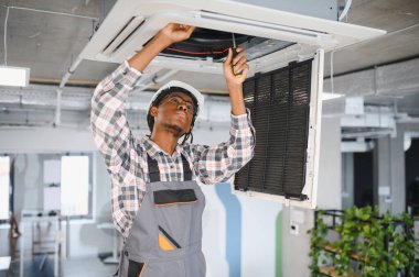 Afrika kökenli Amerikan hvac teknisyeni tavana monte edilmiş klima ünitesi üzerinde çalışırken tornavida kullanıyor.