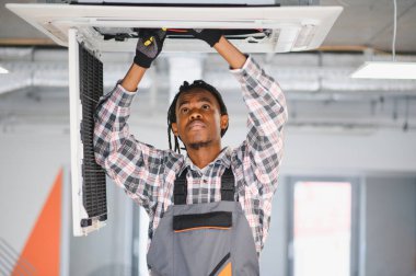 Tavana monte edilmiş havalandırma sistemini inceleyen ve tamir eden Afro-Amerikan HVK teknisyeni