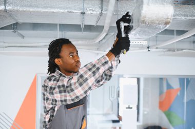 Genç Afrikalı Amerikalı işçi modern bir ofis binasında ingiliz anahtarı kullanarak klima sistemi kuruyor.