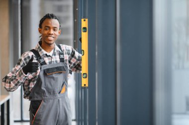 Gülümseyen Afro-Amerikan inşaat işçisi ruhsal seviyesini kullanıyor ve bina tadilatı sırasında işaret ediyor.