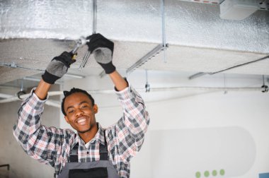 Genç gülümseyen Afrikalı Amerikalı işçi HVC bakımı sırasında havalandırma sistemini sıkıyor.