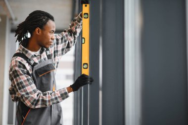 Afrikalı Amerikalı teknisyen havalandırma ve havalandırma sistemleri üzerinde çalışırken doğru hizalamayı sağlamak için bir seviye aracı kullanıyor