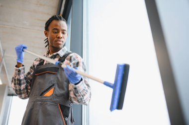 Genç Afro-Amerikan erkek işçi pencereleri siliyor ve modern ofiste eldiven giyiyor.