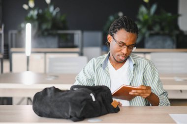 Genç Afrikalı Amerikalı öğrenci üniversite kütüphanesinde kitap okuyor. Konsantrasyon ve adanmışlıkla sınavlara hazırlanıyor.