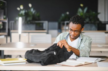 Üniversite kütüphanesinde okurken sırt çantasında araştırma yapan Afrikalı Amerikalı genç bir erkek öğrenci.