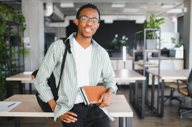 Genç bir Afrikalı Amerikalı öğrencinin portresi, elinde kitaplar ve modern bir üniversite kütüphanesinde gülümseyerek, eğitime ve öğrenmeye hazır.