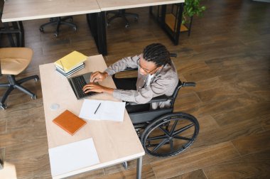 Genç bir Afro-Amerikalı 'nın, tekerlekli sandalyede otururken dizüstü bilgisayar kullanması, kararlılığını pekiştirmesi ve çalışmalarına odaklanması.