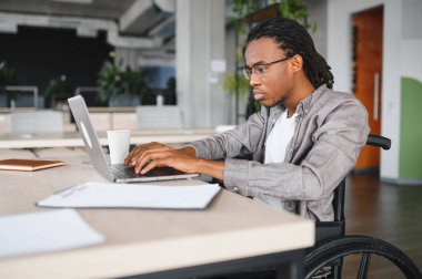 Özürlü genç bir adam modern ofiste dizüstü bilgisayarla çalışıyor, görevlerine odaklanıyor ve kararlılık gösteriyor.