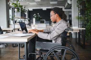 Modern bir ofiste dizüstü bilgisayar kullanan genç bir profesyonel, iş yerine dahil edilme ve erişilebilirliği gösteriyor