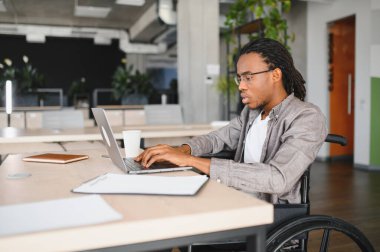 Özürlü genç bir adam dizüstü bilgisayarda çalışıyor, modern işyerine dahil edilme ve erişilebilirlik gösteriyor