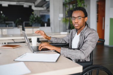 Özürlü genç bir adam modern ofiste dizüstü bilgisayarda çalışıyor, işinden zevk alıyor ve kendini güçlü hissediyor.