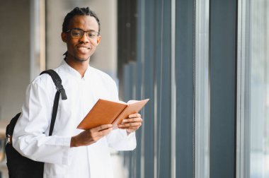 Beyaz önlük giyen, ders kitabı tutan, parlak modern üniversite binasında doktorluk yapan genç bir zenci.