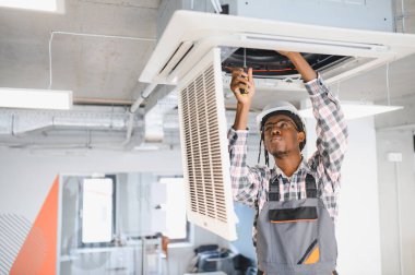 Kendini işine adamış işçiler modern bir ofiste tavan havalandırma ünitesini onarmaya odaklanarak, verimli havalandırma ve kapalı hava kalitesini sağlıyorlar.