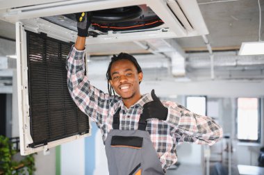 Genç gülümseyen Afro-Amerikan tamirci havalandırma ünitesini tamir ederken HVK bakımı konusunda uzmanlık gösteriyor.