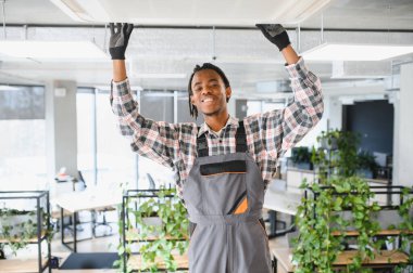 Afrikalı Amerikalı hvac teknisyeni modern bir ofise, rahat bir çalışma ortamı sağlamak için klima sistemi kuruyor.