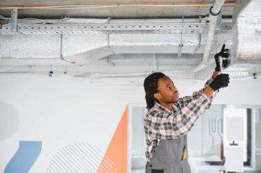 Genç Afrikalı Amerikalı erkek teknisyen ingiliz anahtarı kullanarak havalandırma sistemini tamir ediyor.