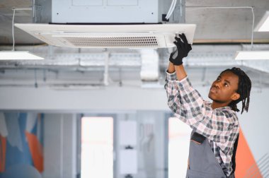Modern ofis ortamında tavana monte edilmiş havalandırma ünitesinin bakımını yapan profesyonel teknisyen en uygun havalandırmayı sağlıyor.