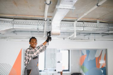 Genç Afrikalı Amerikalı işçiler modern bir ofise klima sistemi kuruyor, uygun iklim kontrolü ve konfor sağlıyorlar.