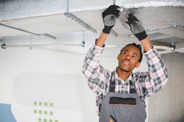 Genç Afro-Amerikan HVK teknisyeni havalandırma ve havalandırma sistemi kurulumu üzerinde çalışıyor.